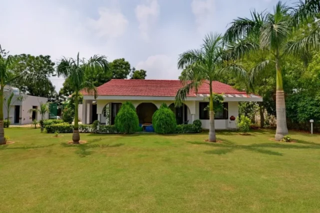 Green Beauty Farms |A Alaska Green Farms located in Sector 135, Noida, Uttar Pradesh, featuring a spacious two-story structure with a tiled courtyard and gated entry. Several bicycles and motorcycles are parked in the open space. Finding your Dream Farmhouse in Noida